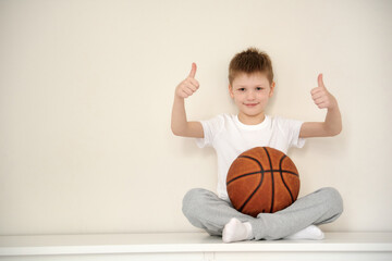 Portret of a little smiling schoolboy sitting at his room, holding a basketbal
