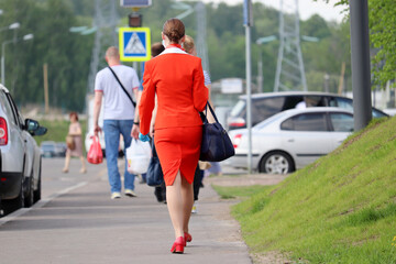 Woman in a red business suit walks down the city street on background of people. Flight attendant after the flight