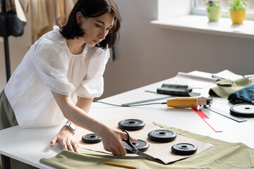 Bespoke garment sewing business concept: young professional dressmaker work with textile in workshop for tailoring fashion collection. Fashion designer seamstress cutting fabric in dressmaking studio
