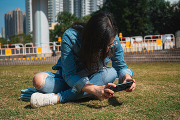 Young woman playing smartphone in summer park wearing denim shirt