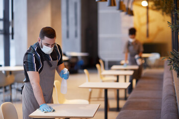 Portrait of male worker wearing mask while cleaning tables in cafe interior, covid safety concept, copy space