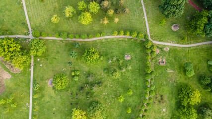 Urban park with meadow, trees and paths. Top view aerial photo from flying drone of a city park with walking path and green zone trees in evening time. - obrazy, fototapety, plakaty