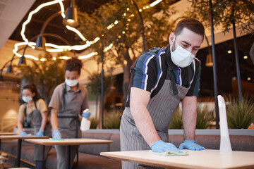 Low angle view at workers wearing masks in row while cleaning tables in cafe interior, covid safety concept, copy space