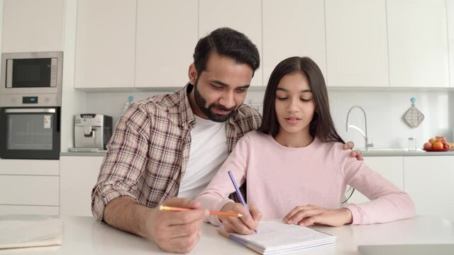 Webcam view of young indian dad helping teenage daughter schoolgirl study online at home sitting at kitchen table at home. Father and kid e learning together having remote distant lesson.
