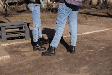 Legs of teenagers in jeans and dark shoes. Spring walk in the park
