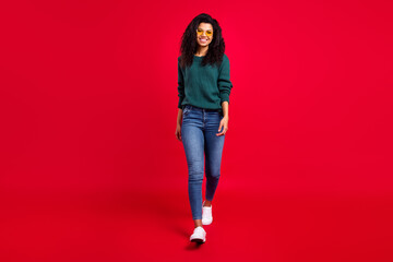 Full size photo of optimistic wavy hairdo lady go wear spectacles sweater jeans sneakers isolated on red color background