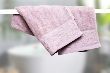 Hanging towels. Closeup of violet pink soft terry bath towels hang on a clothes rail in front of abstract blurred bright gray bath background.