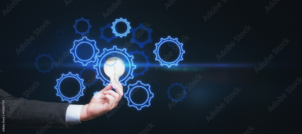 Poster idea concept with man hand carrying glowing light bulb and digital blue gears on abstract blank dark