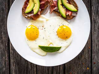 Continental breakfast - sunny side up eggs and crudo sandwiches with avocado on wooden table