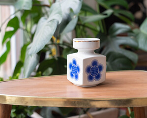 Mid-century modern porcelain vase - geometric shape - on a wooden table with plants in the background
