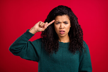 Photo of unhappy young dark skin woman point finger temple displeased expression isolated on red...