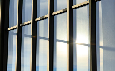 Background of modern exterior design and architecture of glass window building with reflection of blue sky, clouds and sunlight in the evening time.