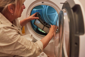 Hausfrau reinigt das Flusensieb von Waschmaschine