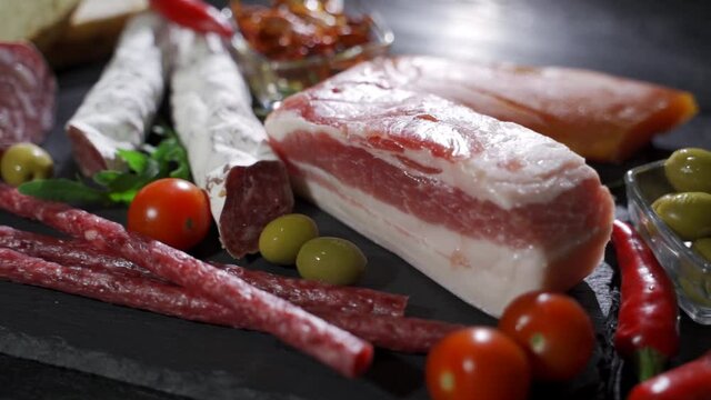 Ham, sausage, tomatoes and various vegetables on a black table. Meat products with vegetables. Delicious appetizer close-up. Camera moves from right to left.
