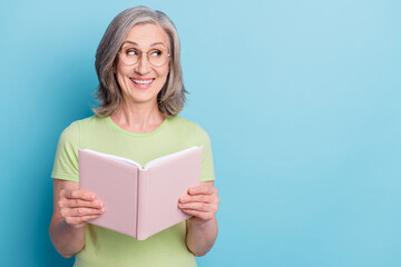 Photo of charming dreamy happy old woman hold book novel look empty space isolated on blue color...