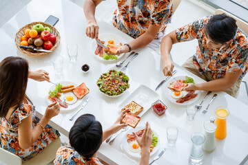 Top, aerial view Asian family sitting and having breakfast, bread with jam, taking care of each other in a bright refresh morning at table in comfortable dining room at home with happiness and warmth.