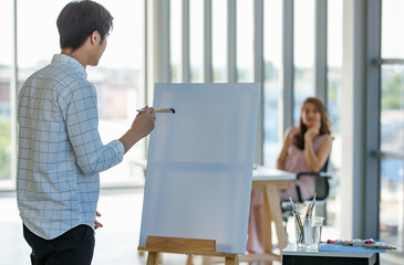 Portrait 20s young Asian male artist drawing and painting art picture of woman posing as role model...