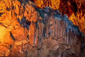 Naklejka premium Mineral formations on the walls of Damlatas cave in Alanya (Turkey), close-up. Abstract geological natural background in yellow-brown-blue colors