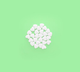 White pills in the shape of hearts on a pastel green background