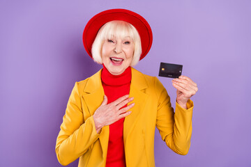 Portait of impressed short hairdo senior lady show card wear yellow jacket cap isolated on purple background