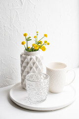 White home decoration with yellow flowers, ceramic vase and glass on tray