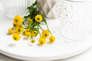 White home decoration with yellow flowers, ceramic vase and glass on tray