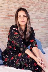 A happy girl rests on the sofa for a chill out, smiles at the camera. She wears a flowery dress and long nails.