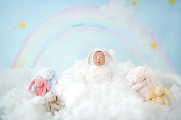 Baby newborn wearing white swaddling wrap standing on white cloud. Newborn is between five rabbit...