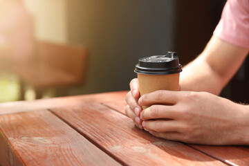 Fototapeta na wymiar Man with takeaway coffee cup at wooden table outdoors, closeup. Space for text