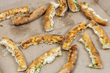 Pizza crusts in a greasy box on a home table. Leftover pieces of pizza. Close-up high-calorie food