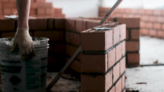 Mason employee in gloves applies concrete mix on bricks making wall in spacious hall at construction site extreme close view