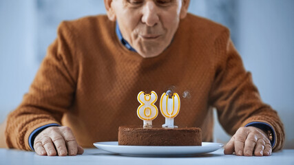 cheerful elderly man blowing out candles on birthday cake on grey background. - Powered by Adobe