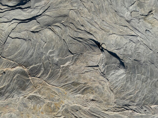 Volumetric texture of gray stone with layers washed by the sea and wind with shadows and light.