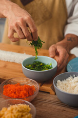Close up male chef's hands adds ingredients to sushi rolls. Food delivery online service. Background for menu