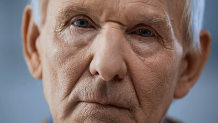 close up view of elderly man looking at camera on grey background.