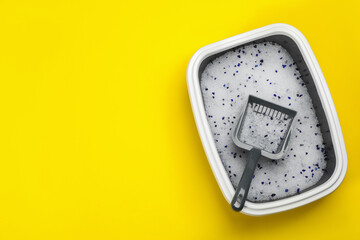 Cat litter tray with filler and scoop on yellow background, top view. Space for text