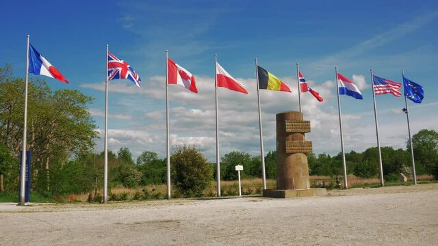 Caen, France May 2021. Time lapse multi-country flags in the wind next to a WWII memorial at Pegasus Bridge in Caen. 4k high definition movie