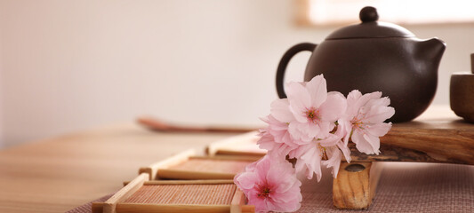 Pot, sakura flowers and bamboo coasters for traditional tea ceremony on table. Banner design