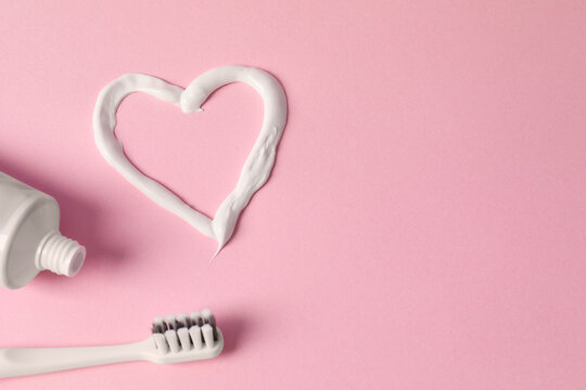 Heart made with toothpaste, tube and brush on pink background, flat lay. Space for text