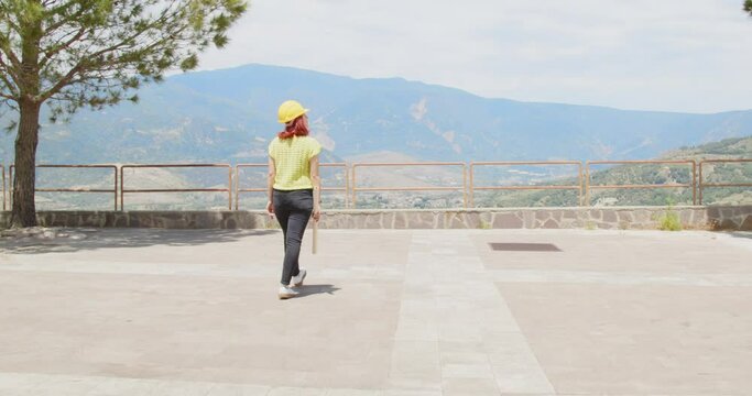 Giovane ragazza architetto va ad un affaccio panoramico in montagna con un progetto in mano
