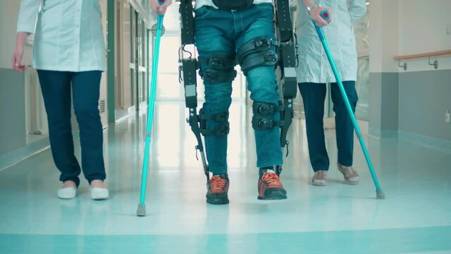 Hospital hall with a man walking in the exoskeleton with assistance