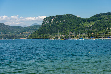 Fototapeta premium Large group of sailing boats moored in front of the small village of Bardolino, coast of Lake Garda (Lago di Garda) with the hill called Rocca di Garda. Verona province, Veneto, Italy, southern Europe