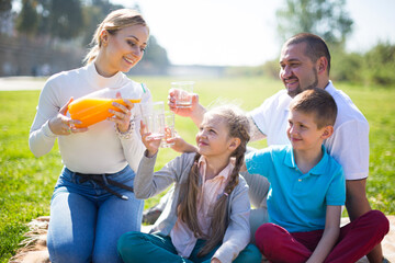 young woman treating orange juice to her family at picnic