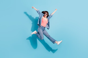 Full size photo of joyful young lady jump wear top jeans eyewear isolated on blue color background