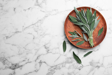 Wooden plate with fresh green sage on white marble  table, flat lay. Space for text