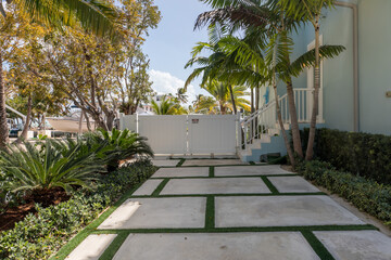 Modern Concrete slabs separated by grass in driveway with white fence.