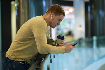 young man using smartphone and listens to music in bluetooth headphones. lonely man in autumn...