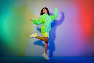 Full length body size view of beautiful trendy cheerful girl jumping showing v-sign isolated over multicolor vivid neon light background