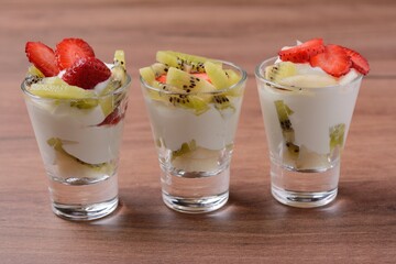 Berry dessert smoothie made of strawberry slices and yogurt in small glasses, against the background of a wooden structure, close-up