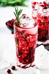 Cranberry, vodka, gin alcoholic cocktail with ice, rosemary and berries in highball glass. Summer long drink. Gray table background